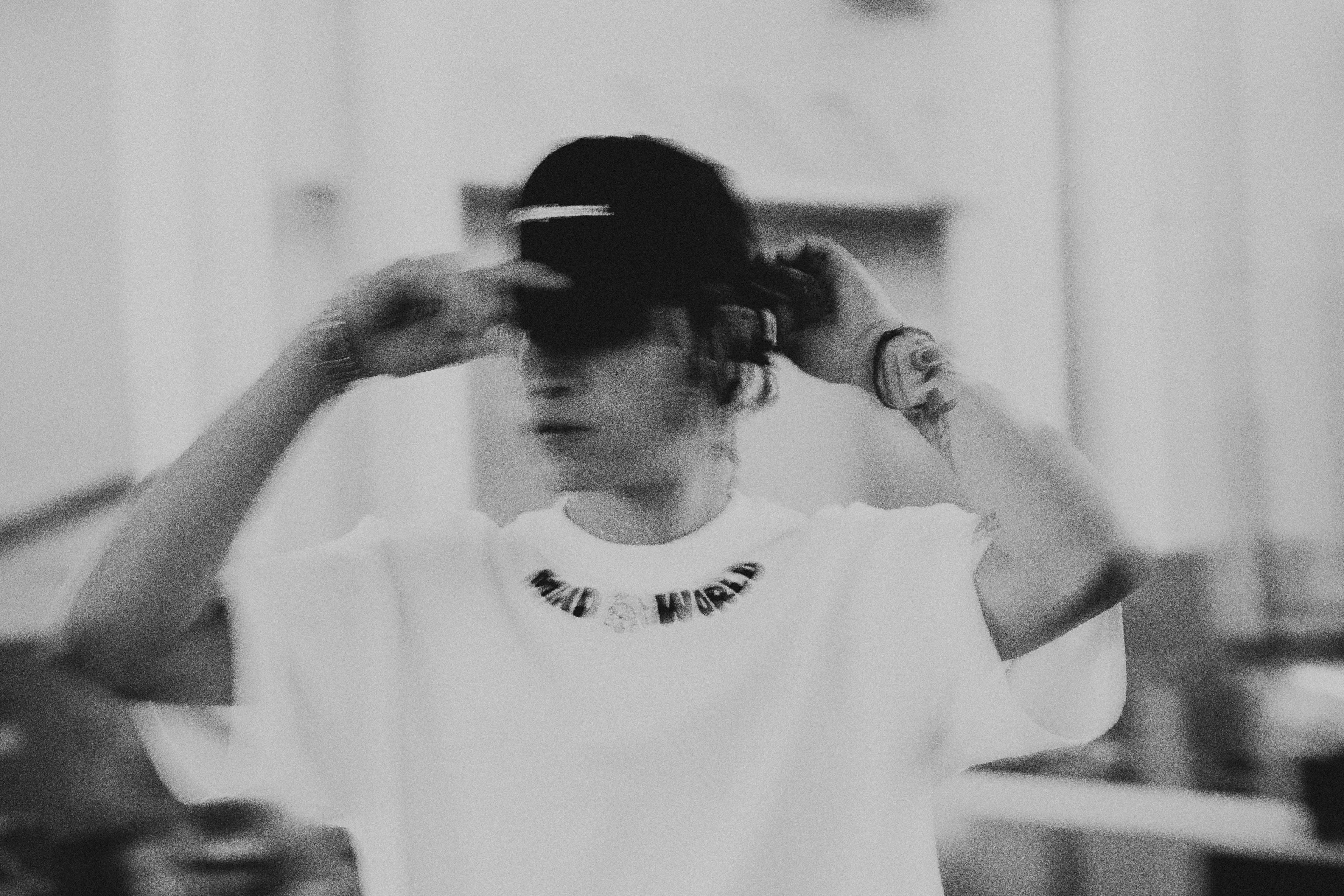 Person wearing a white t-shirt with text, adjusting a cap indoors.